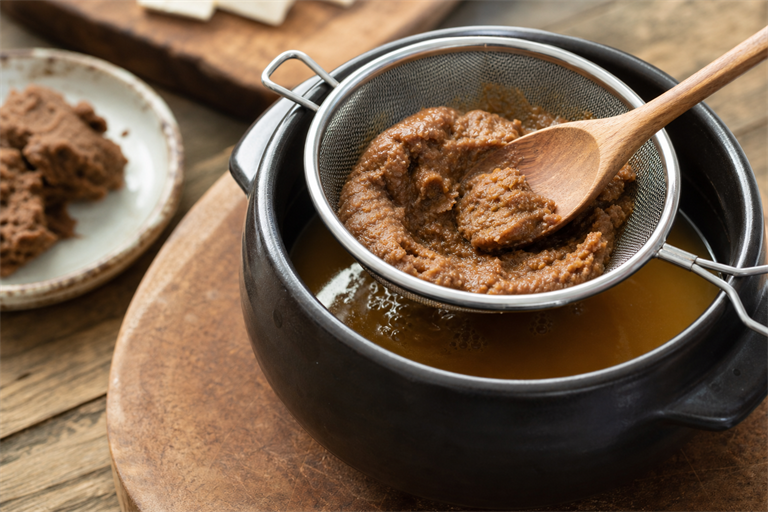 Step 2: a small fine-mesh strainer set over a black ttukbaegi clay pot with dark brown d