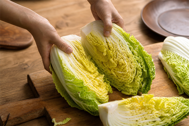 Step 1: a whole napa cabbage being torn into quarters by hand on a wooden board, leaves