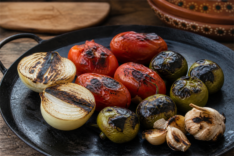 Step 3: halved white onion unpeeled garlic plum tomatoes and tomatillos charring on a bl