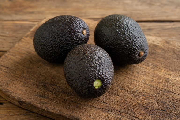 Step 1: three ripe hass avocados on a rustic wooden board with one stem cap flicked off 