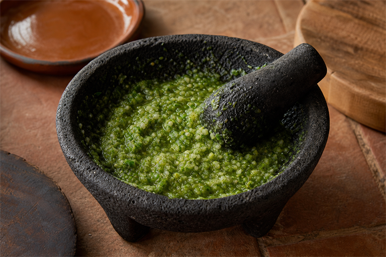 Step 2: a dark volcanic basalt molcajete with a green wet paste of salt onion serrano an