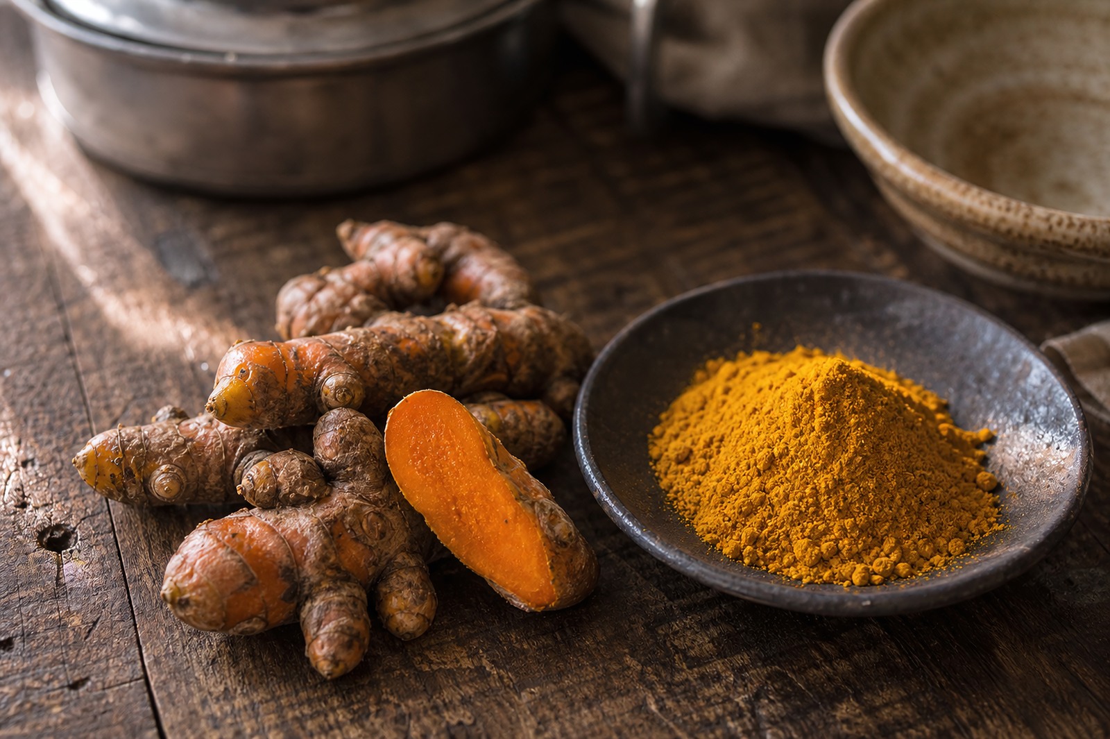 Fresh turmeric rhizomes beside a mound of vivid yellow turmeric powder